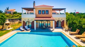 Ein zweistöckiges Haus mit Swimmingpool, Sitzgelegenheit im Freien und Blick auf die umliegende Grünfläche.