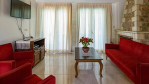 Ein Wohnzimmer mit einem roten Sofa, einem Holztisch mit einem Blumentopf, einem Flachbildfernseher und einem Kamin aus Stein.