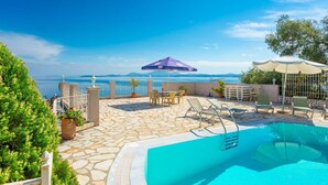 Un espace piscine offrant une vue dégagée sur la mer, avec un sol en pierre et des espaces de détente en plein air agrémentés de parasols.