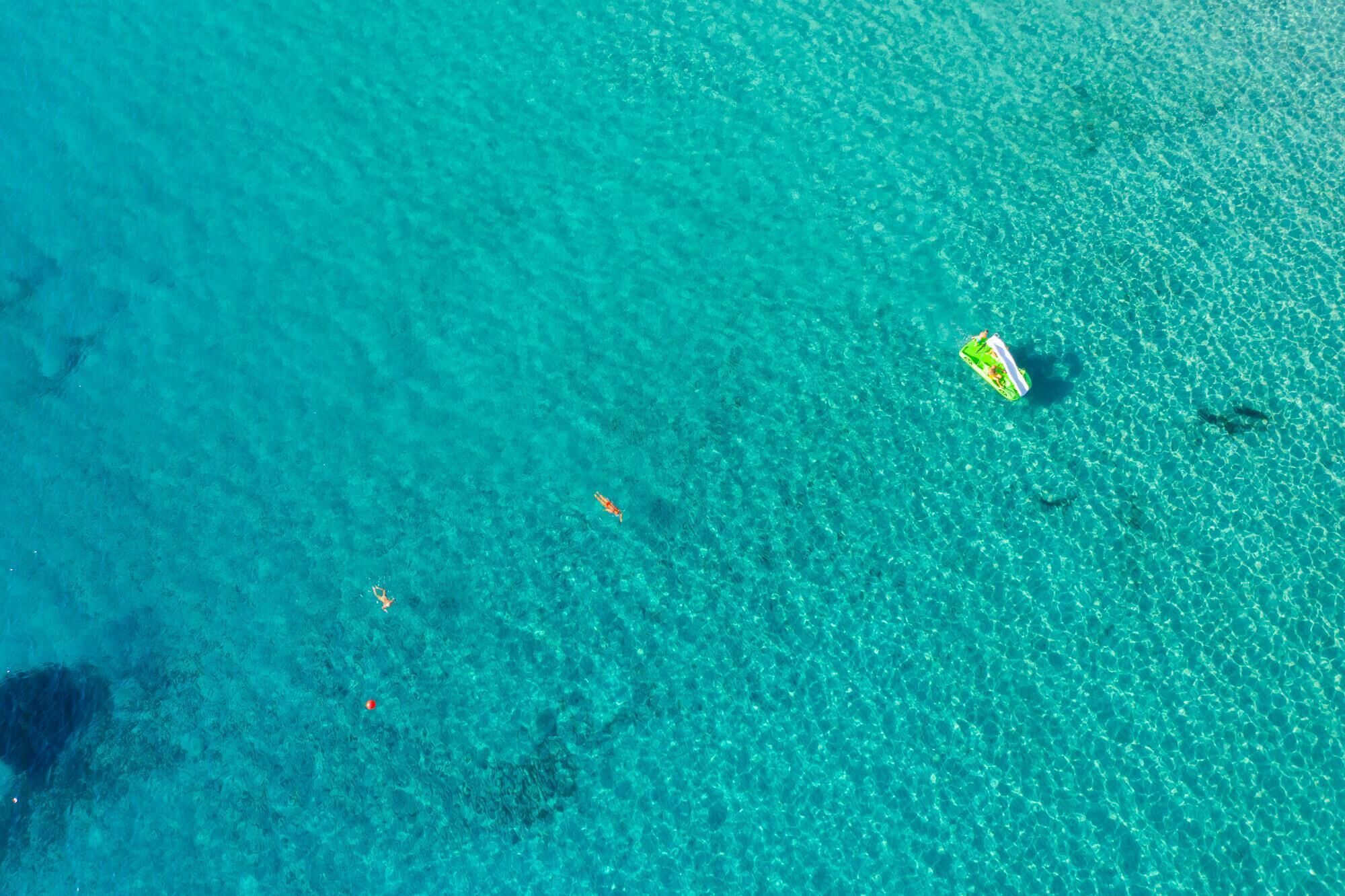 A clear turquoise sea with a small green and white boat floating on the surface.
