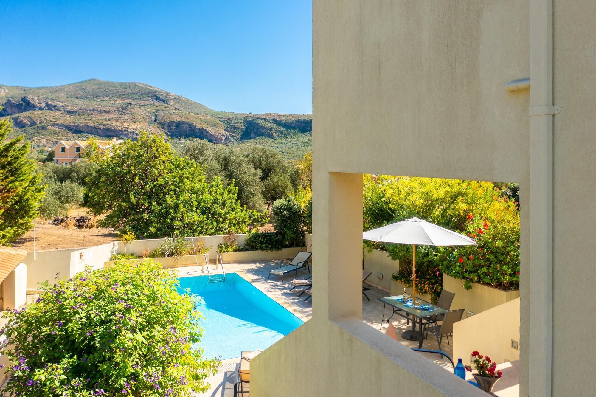 A pool with a view of a mountain, surrounded by greenery and a patio area with outdoor furniture.