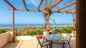 A balcony with a view of the sea, a round table with chairs, and a pergola structure.