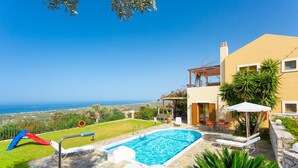 A swimming pool with lounge chairs and a slide, surrounded by a stone patio and a view of the sea.