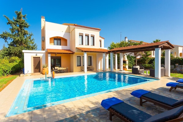 A modern villa with a swimming pool, outdoor seating, and a covered patio area.