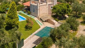 Une maison à deux étages avec une façade en pierre, un toit recouvert de tuiles rouges et une piscine.