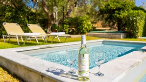 Un cadre agréable au bord de la piscine, avec une bouteille de vin et des verres, entouré de chaises longues et de verdure.