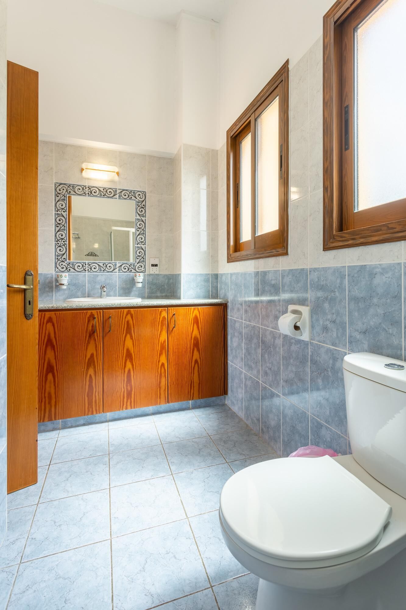Une salle de bain avec un meuble-lavabo en bois, des toilettes blanches et un miroir doté d’un cadre décoratif.