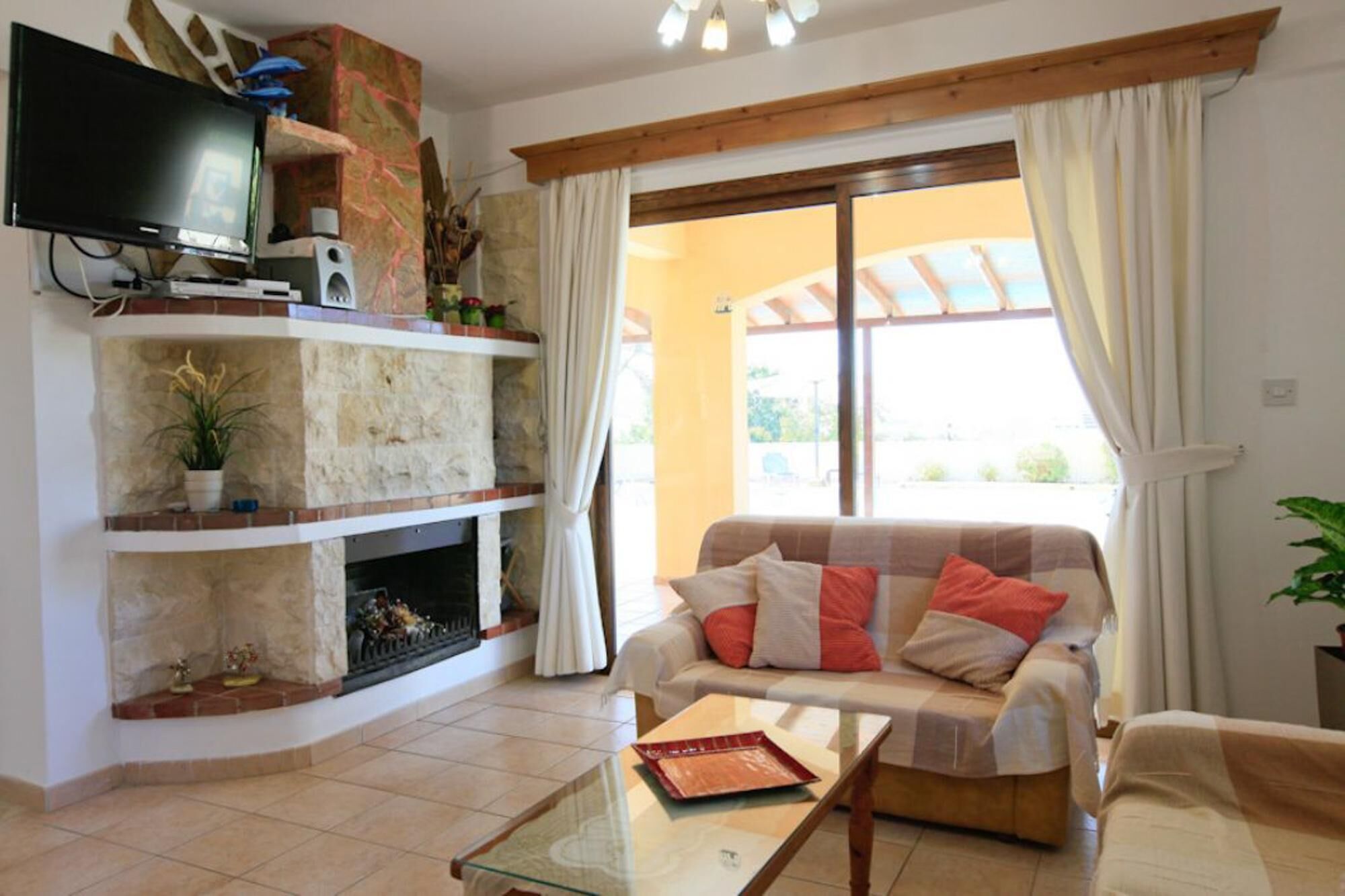 A living room with a stone fireplace, a flat-screen TV mounted above it, a sofa with cushions, and a glass coffee table.