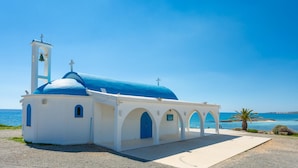Una iglesia blanca con una cúpula azul y un campanario junto al mar.