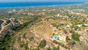 Luftaufnahme einer Küstenregion mit hervorgehobenem Anwesen, das einen Swimmingpool, Olivenhaine und eine hügelige Landschaft umfasst.