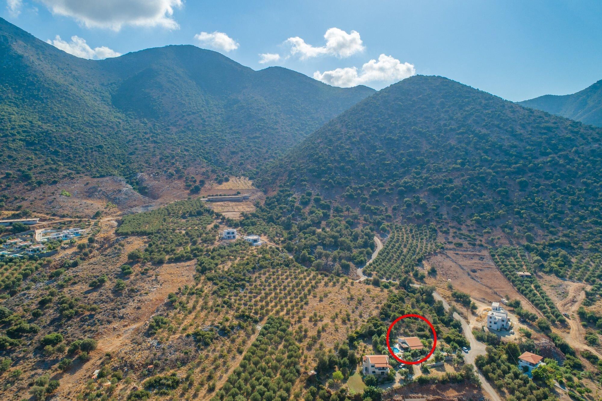 An aerial view of a mountainous area with scattered buildings, a winding road, and a circled property.