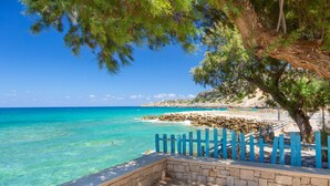 A coastal view with clear turquoise waters, a stone pathway, and a blue fence leading to a beach.