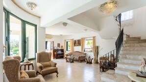 A spacious living area with a grand staircase, a piano, and a dining area. - Villa Charianna Large Private Pool Walk to Beach Sea Views A C Wifi Car Not Required Eco-frie - 1985 (Ayia Marina Chrysochous)