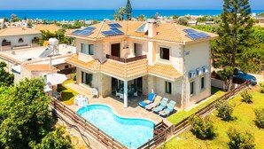 Una casa de dos pisos con piscina, paneles solares y vista al mar.