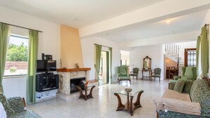 Amplia sala de estar con chimenea, muebles tapizados en verde y una escalera que conduce a otro nivel.