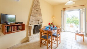 A living room with a fireplace, a television, a bookshelf, and a dining area with blue tableware. - Villa Russa Dionisis Large Private Pool Walk to Beach Sea Views Wifi Car Not Required - 2017 (Kefalonia)