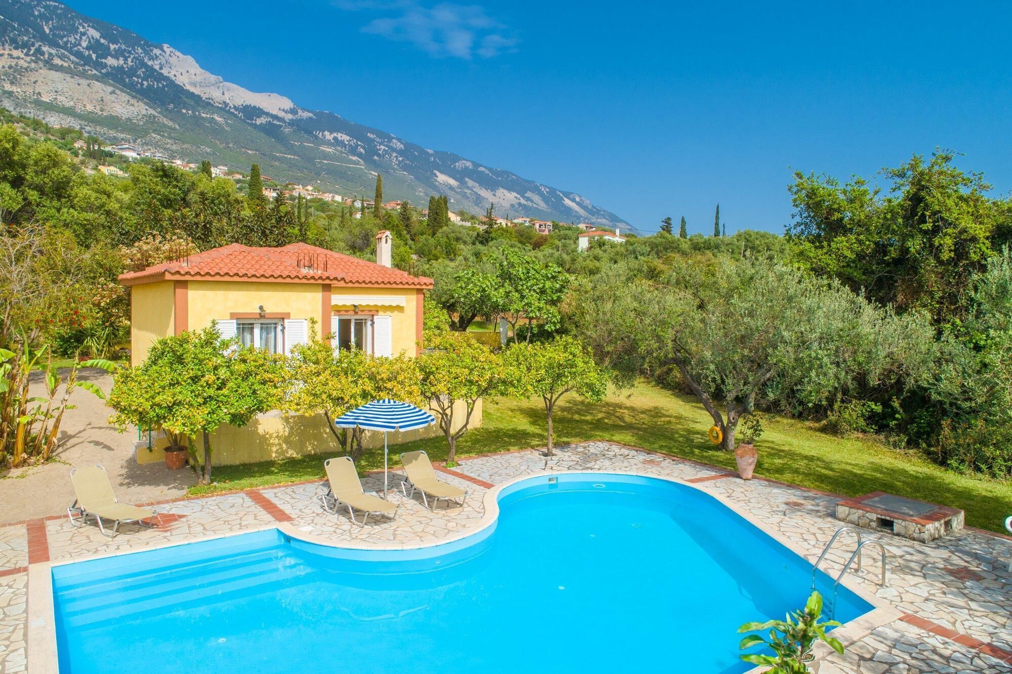 A pool area with a house, a mountain backdrop, and a clear sky.