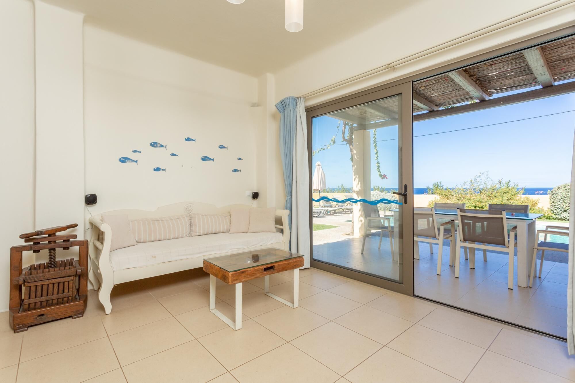 Quarto com sofá branco, mesa de centro de vidro e vista para o mar através de uma porta de correr.