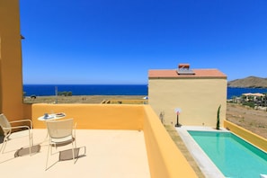 Enjoy breathtaking views of the sea and distant mountains from this balcony, featuring a pool, sun lounger, and comfortable seating.