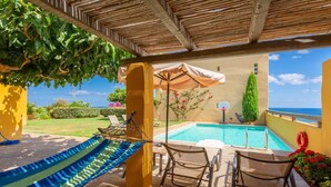 A poolside area with a hammock, two chairs, a sun umbrella, and a view of the sea. - Villa Liakada Large Private Pool Walk to Beach Sea Views A C Wifi Car Not Required - 2081 (Mylopotamos)