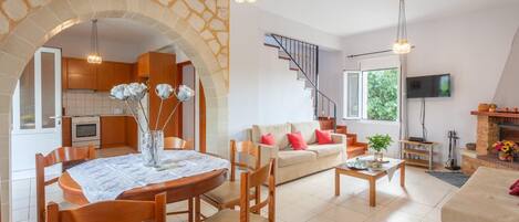 A spacious living area with a stone archway, wooden furniture, a sofa, and a TV mounted on the wall.