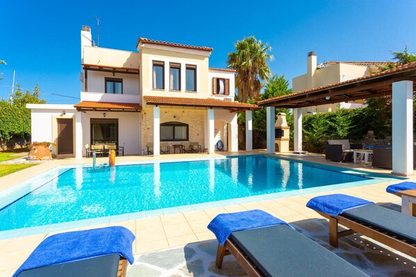 Una casa de dos pisos con piscina, mobiliario exterior y una pérgola.