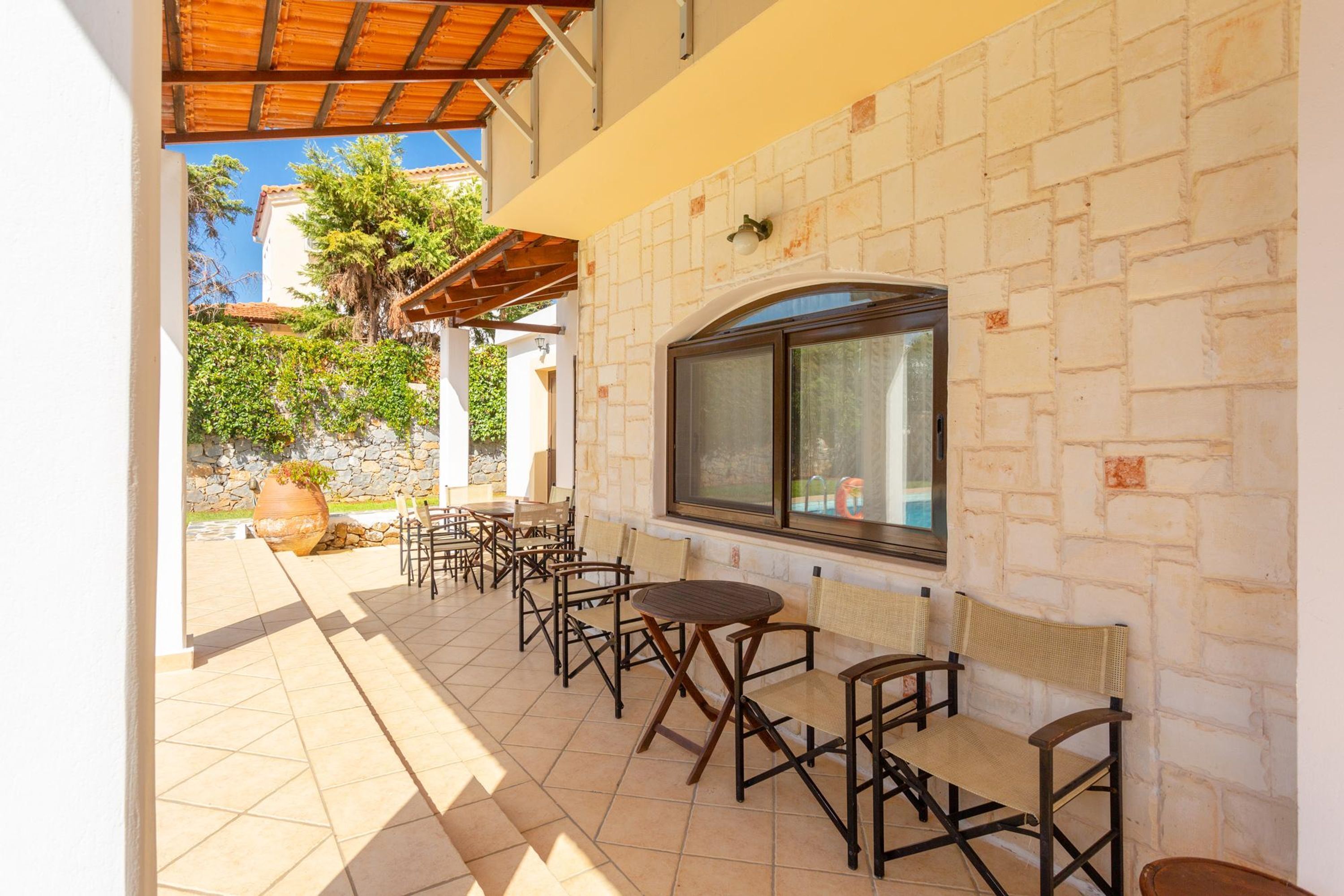 Un patio al aire libre con varias mesas y sillas, un muro de piedra y una ventana con vistas a un jardín.