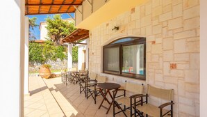 Une terrasse extérieure avec plusieurs tables et chaises, un mur en pierre et une fenêtre donnant sur un jardin.