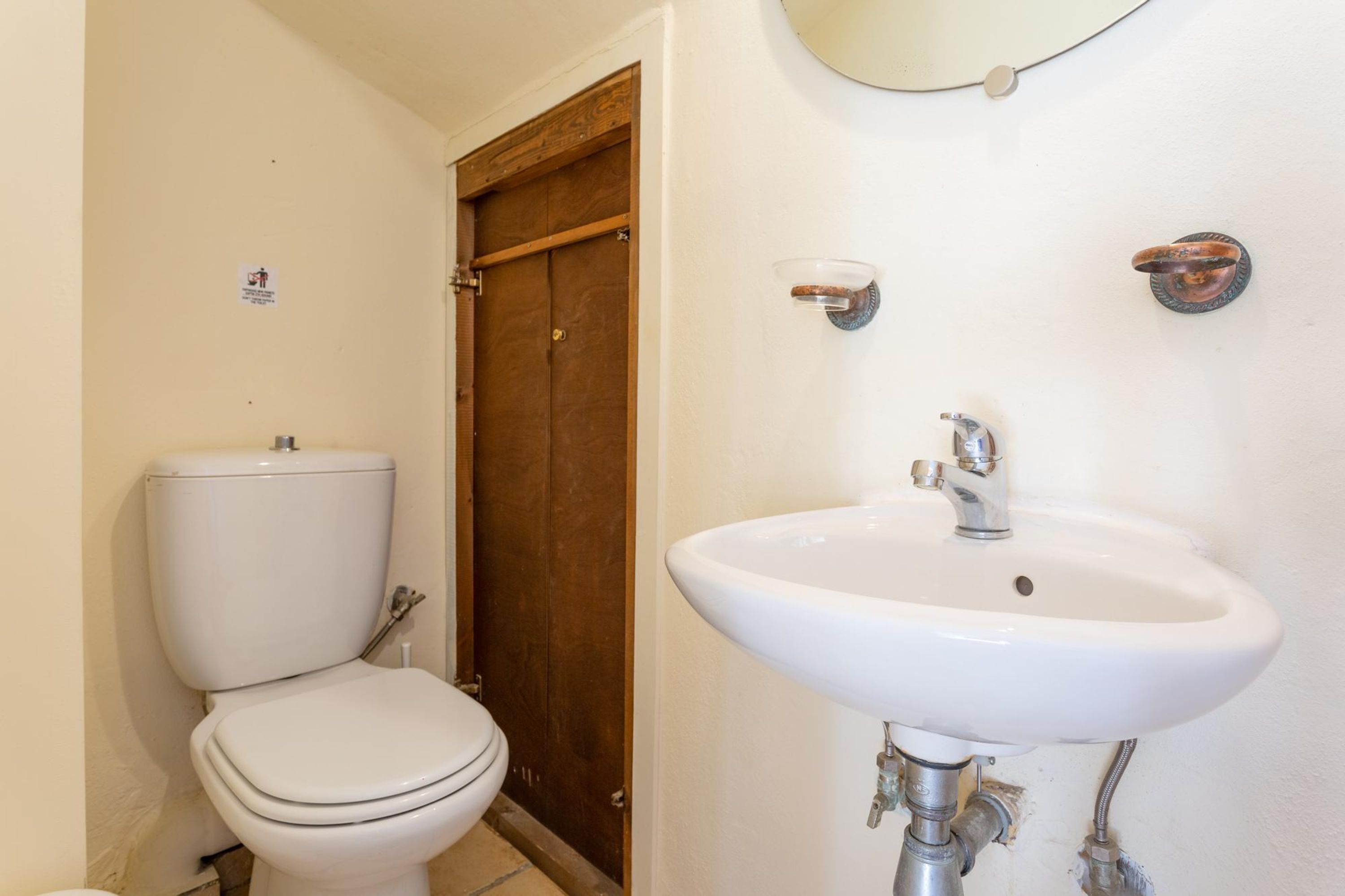 Ein Badezimmer mit Toilette, Holztür und Waschbecken mit Spiegel darüber.