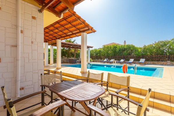 A poolside area with a covered seating area, a pool, and lounge chairs.