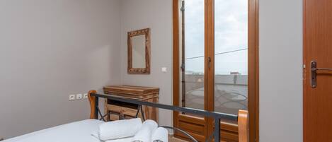 Une chambre à coucher comprenant un lit, une commode en bois, un miroir et une porte-fenêtre coulissante donnant sur un balcon.