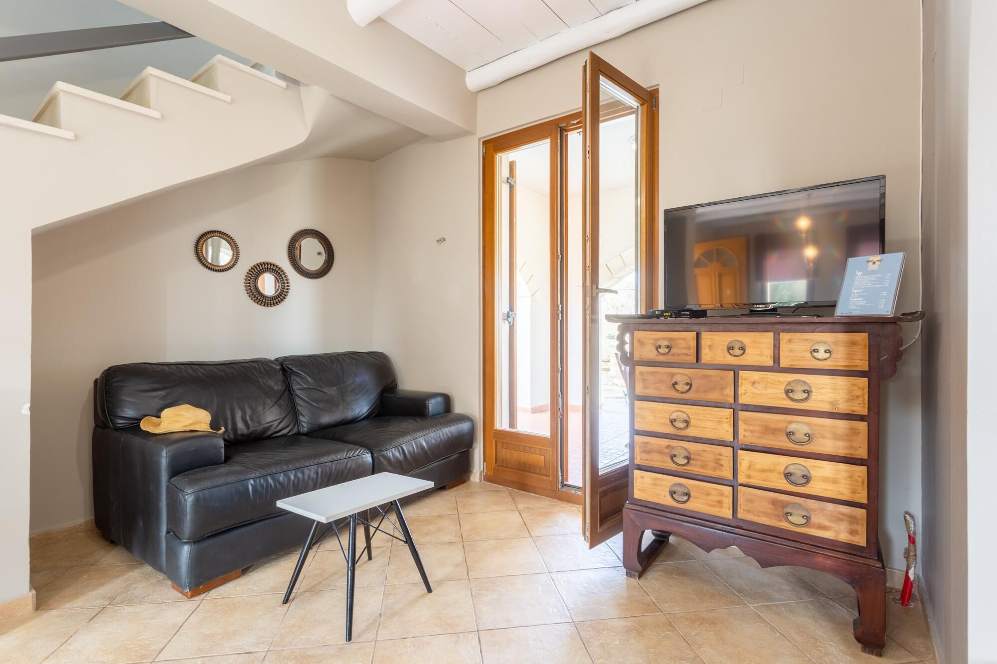 A living room with a black leather sofa, a white coffee table, and a wooden dresser with drawers.