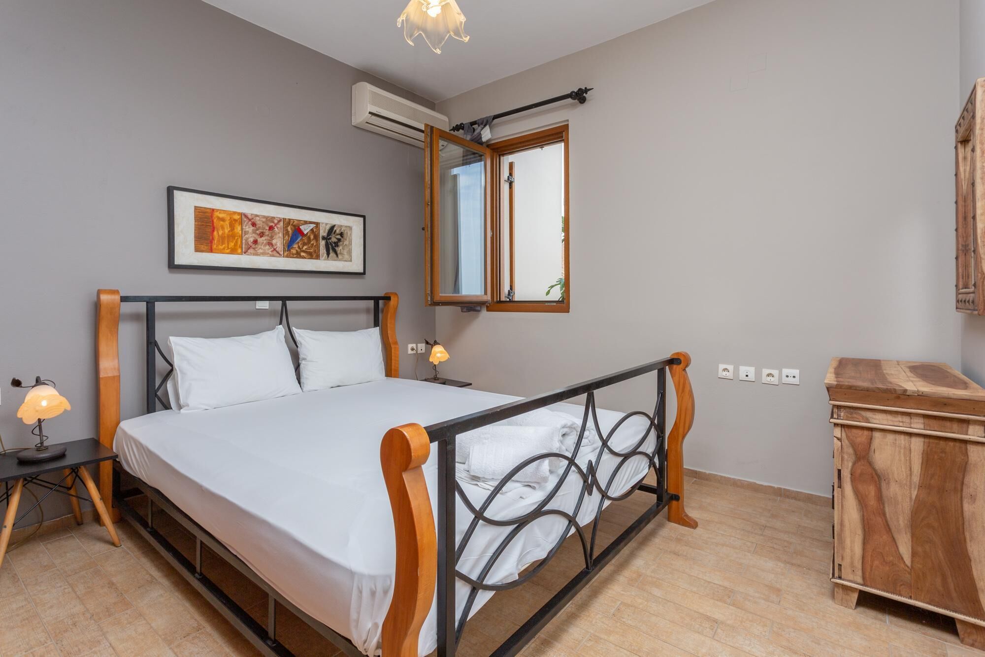 Une chambre à coucher comprenant un lit, des lampes de chevet, une armoire en bois, une fenêtre avec vue et un appareil de climatisation.