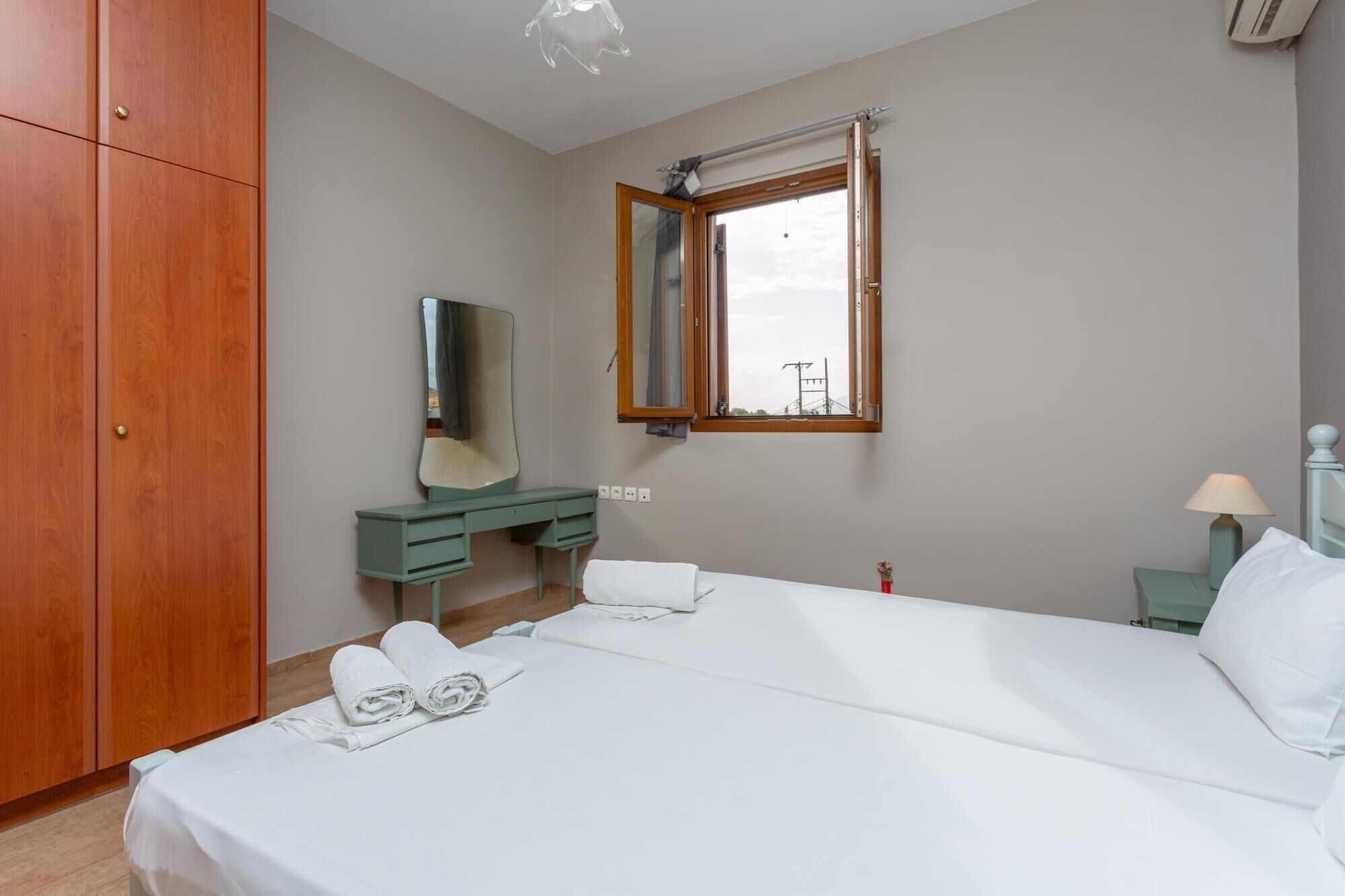 Een slaapkamer met een bed, een houten kledingkast, een kaptafel met spiegel, een raam en een bedlampje.