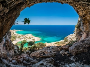 A view through a cave opening to a coastal landscape with clear turquoise waters and a sandy beach. - Souda Bay View Large Private Pool Walk to Beach Sea Views A C Wifi - 2119 (Chania)