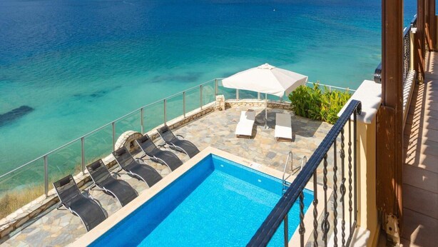Zona de piscina con agua cristalina, vistas al mar y una terraza de madera.