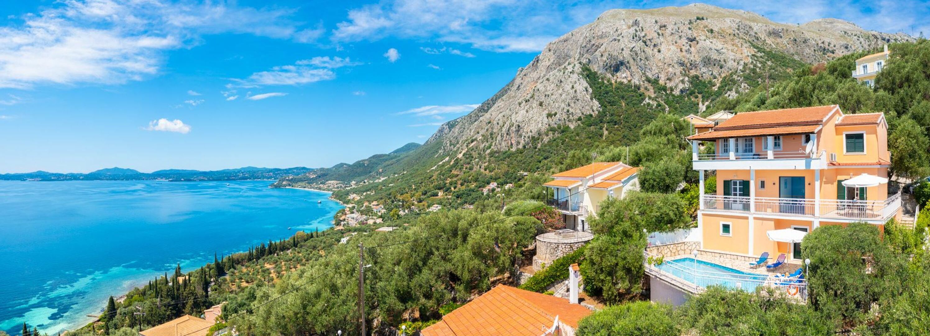 A coastal property with a mountain backdrop, a swimming pool, and a view of the sea.