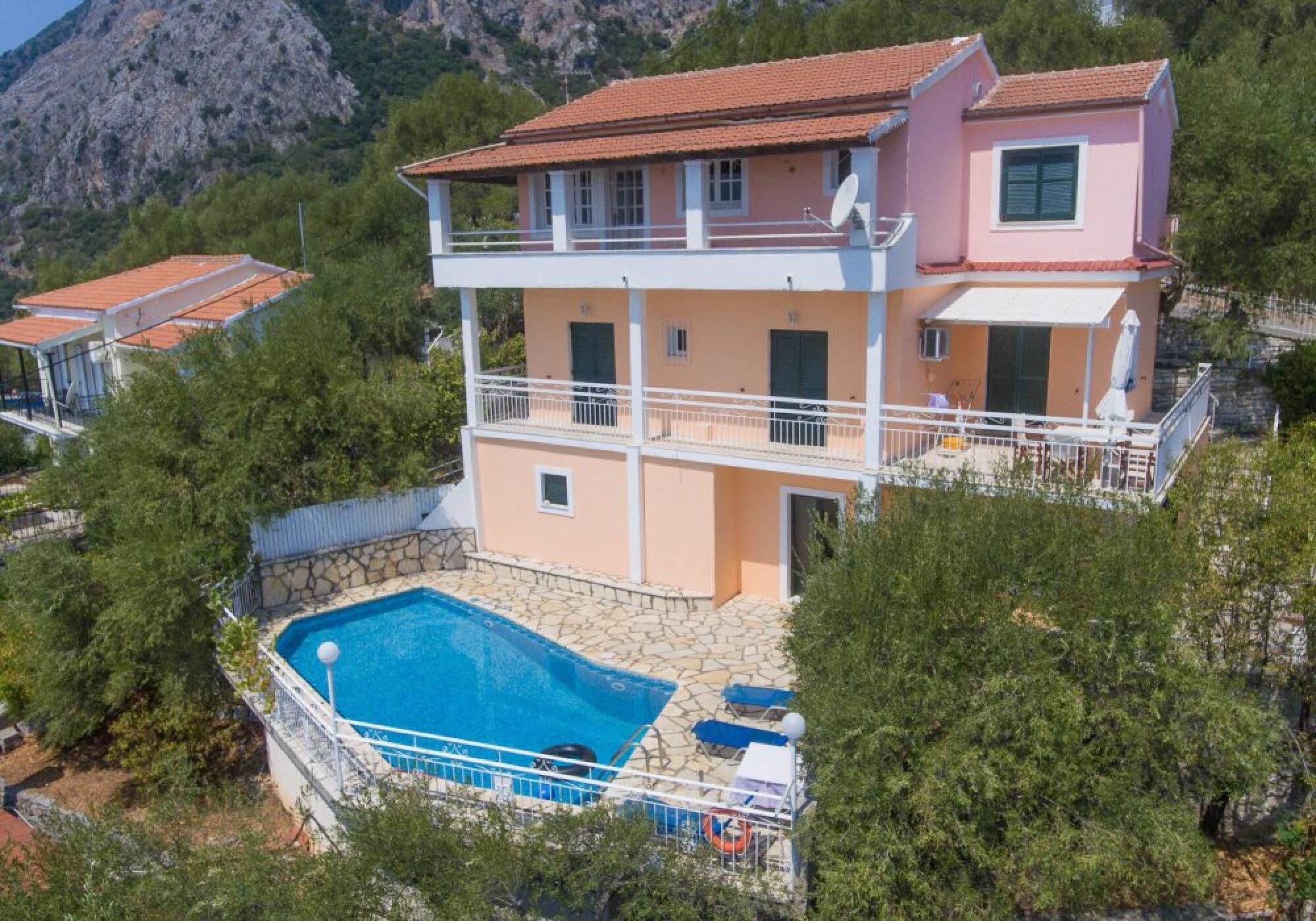 A two-story house with a swimming pool, surrounded by trees and mountains.