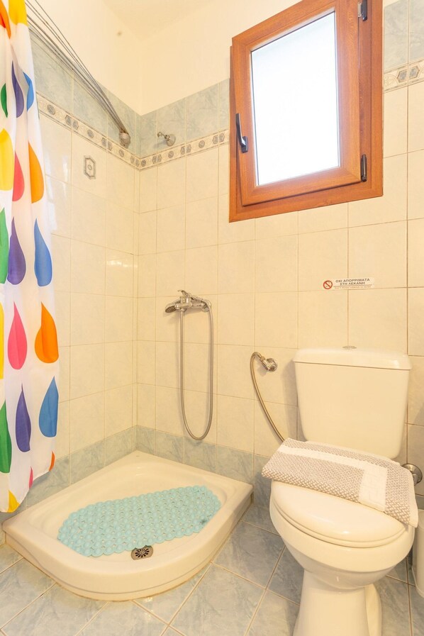 A bathroom with a shower, toilet, and a window.
