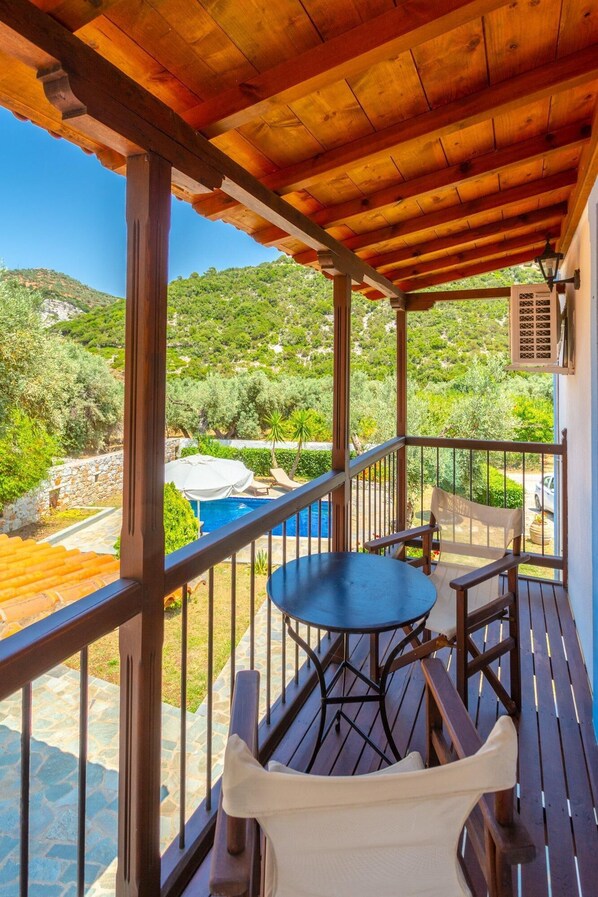 A wooden deck with a table and chairs, overlooking a pool and lush greenery.