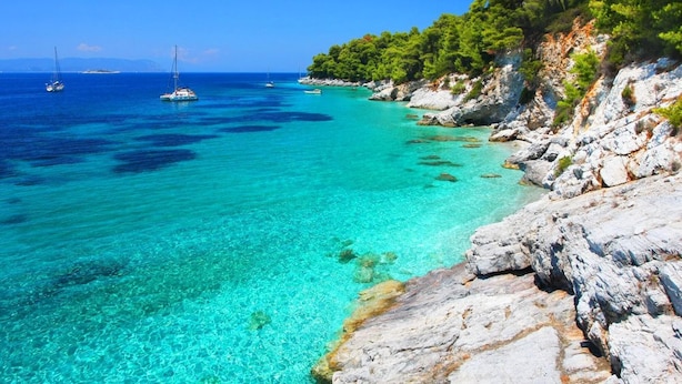 Un paysage côtier caractérisé par une eau turquoise et limpide, des rivages rocheux et des bateaux visibles au loin.