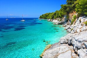 A coastal landscape with clear turquoise waters, rocky shorelines, and boats in the distance.
