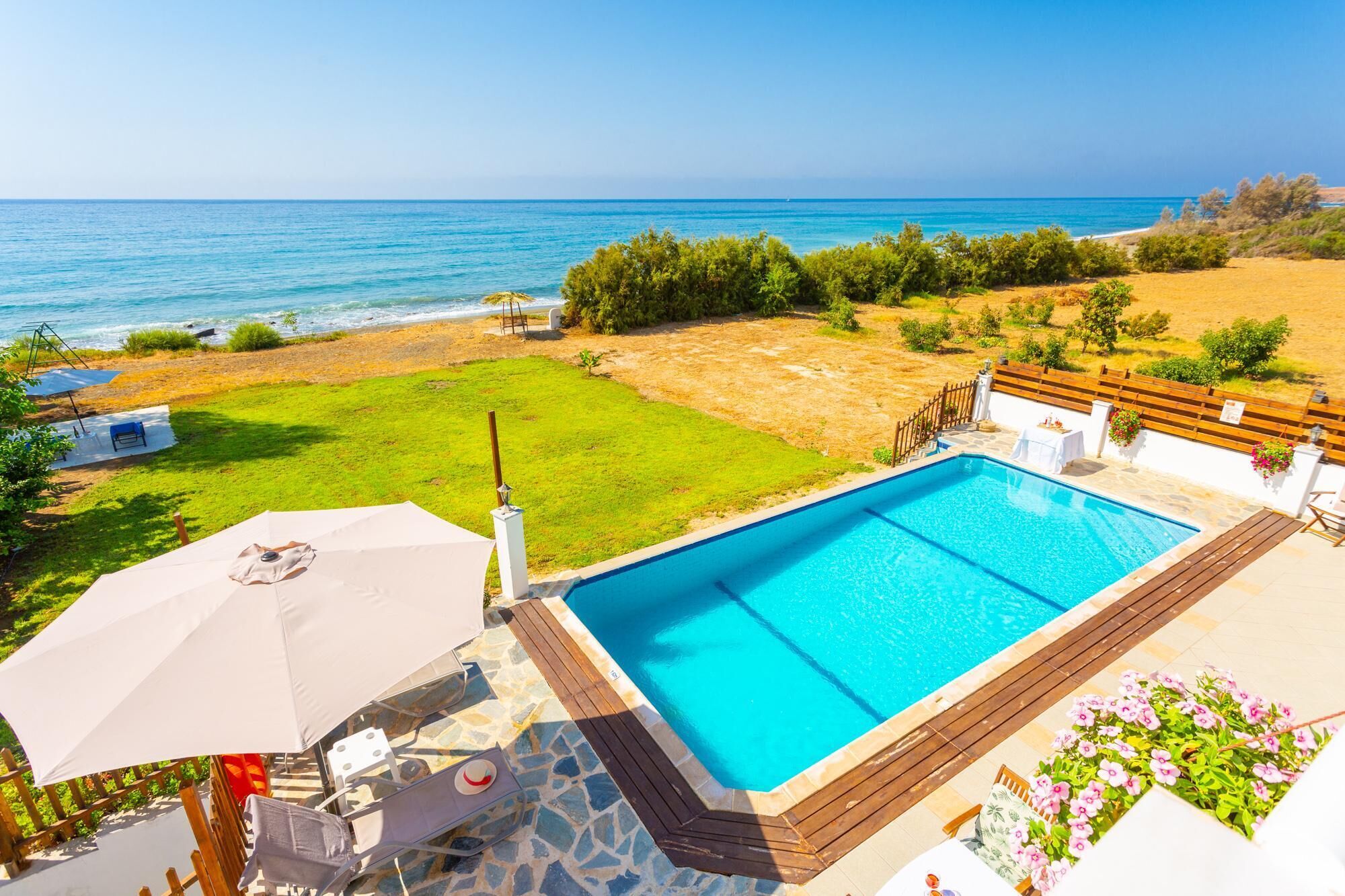 A swimming pool with a view of the sea, surrounded by a grassy area and a wooden deck.