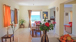 A spacious living area with a view of the sea, a dining area, and a bedroom with a red bed. - Kalisto Beach Villa Large Private Pool Walk to Beach Sea Views A C Wifi Car Not Required - 2137 (Ayia Marina Chrysochous)