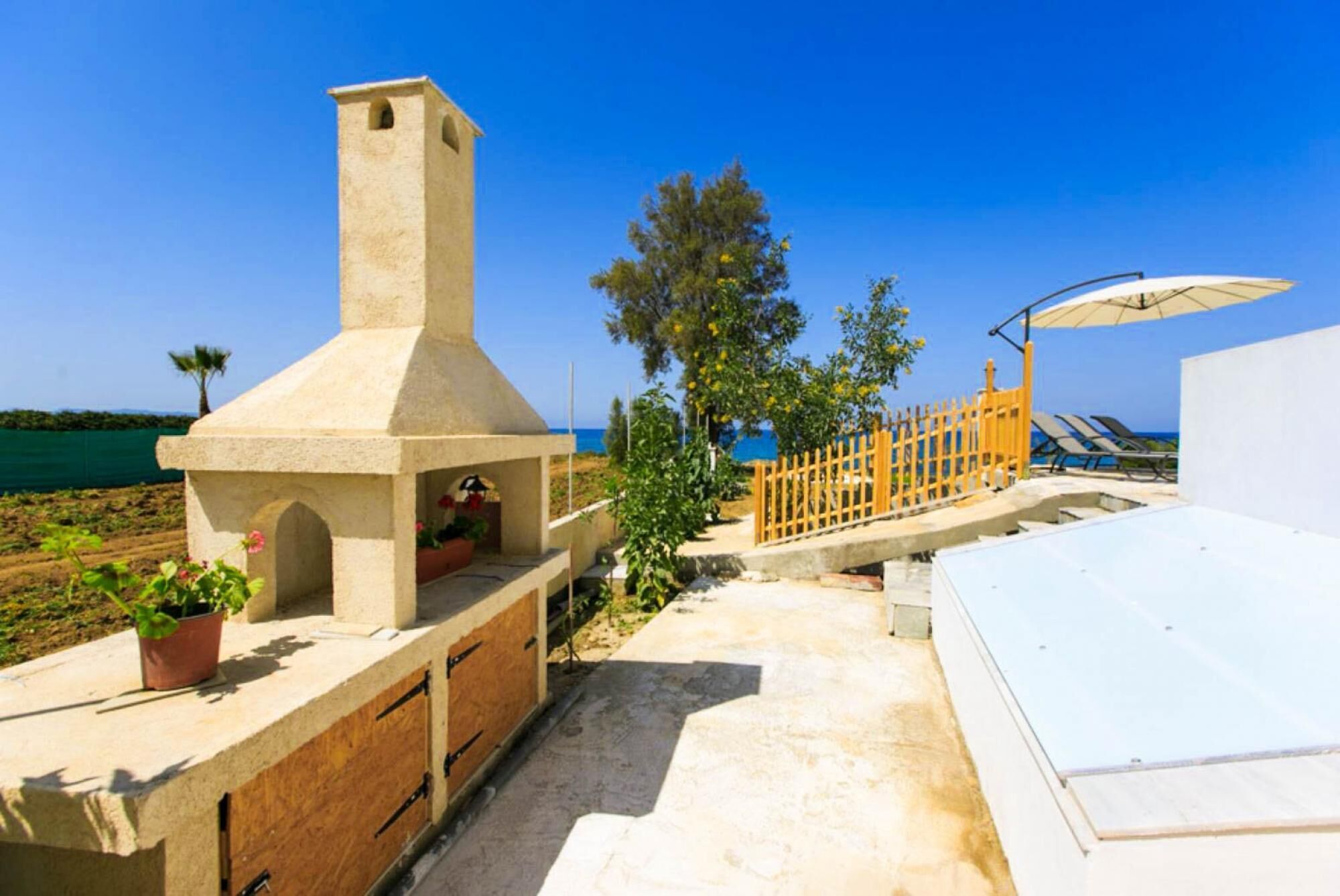 Une terrasse avec un barbecue en pierre, une clôture en bois et une vue sur la mer.
