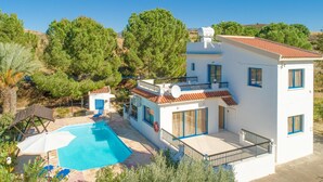 Une maison à deux étages avec une piscine, entourée d’arbres et de collines.