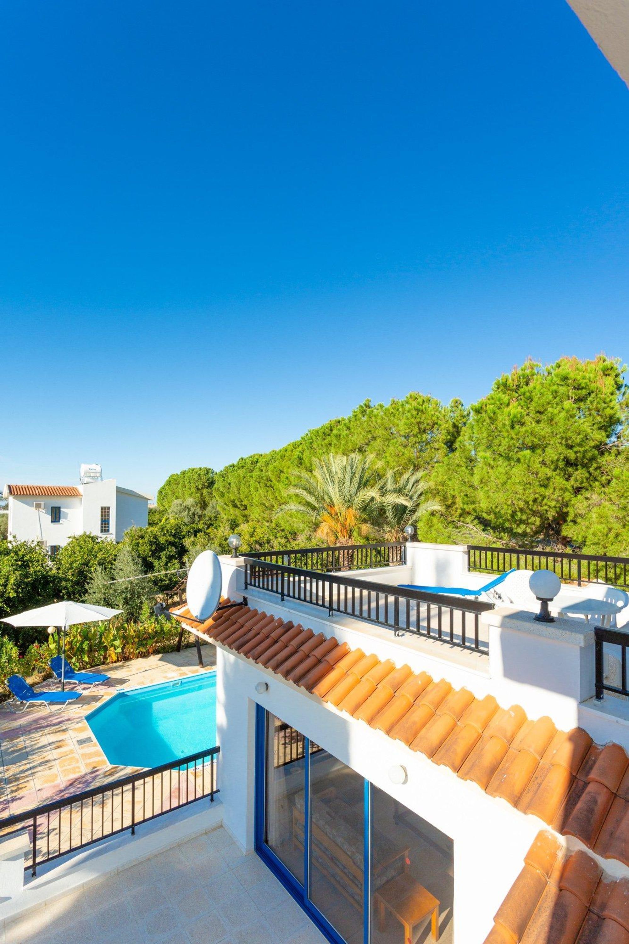 A modern building with a rooftop pool, a balcony with a railing, and a view of a lush green landscape.