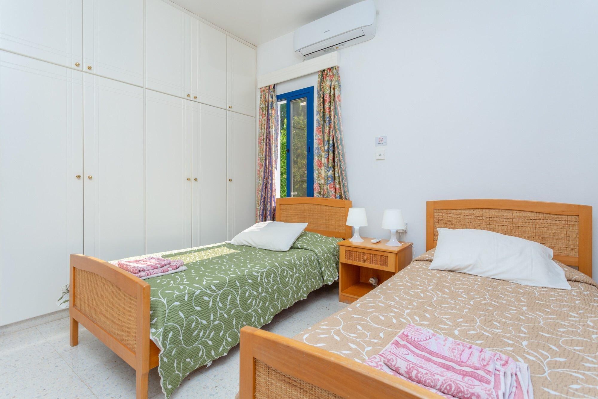 A bedroom with two single beds, a wardrobe, a nightstand, and a window with curtains.