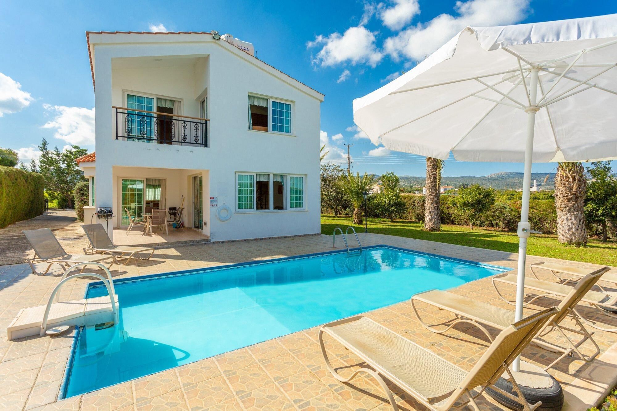 A two-story white house with a swimming pool, outdoor furniture, and a view of the landscape.