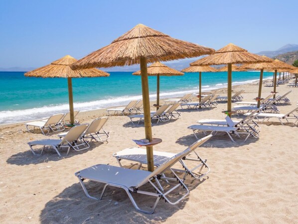A beach with sun loungers and thatched umbrellas.